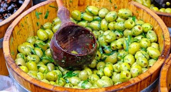 Marinated green olives in a wooden barrel with a serving ladle